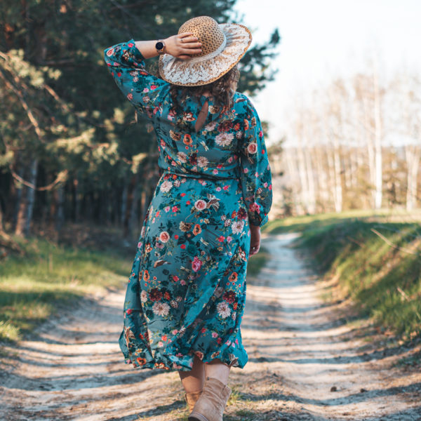 Kobieta idąca leśną ścieżką, w sukience i kapeluszu ze smartwatchem Garett na ręce
