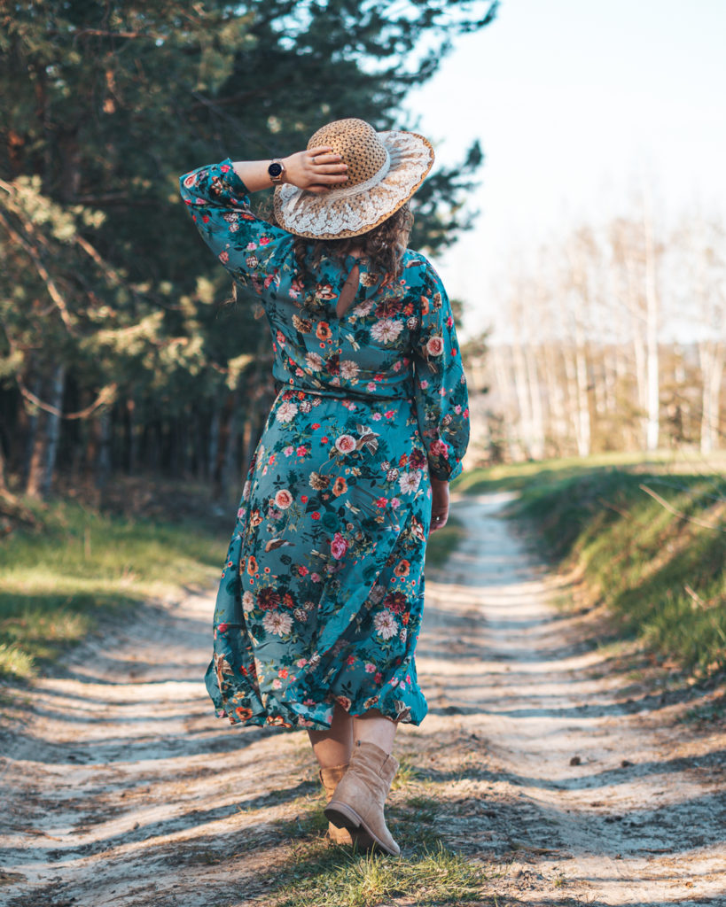 Kobieta idąca leśną ścieżką, w sukience i kapeluszu ze smartwatchem Garett na ręce